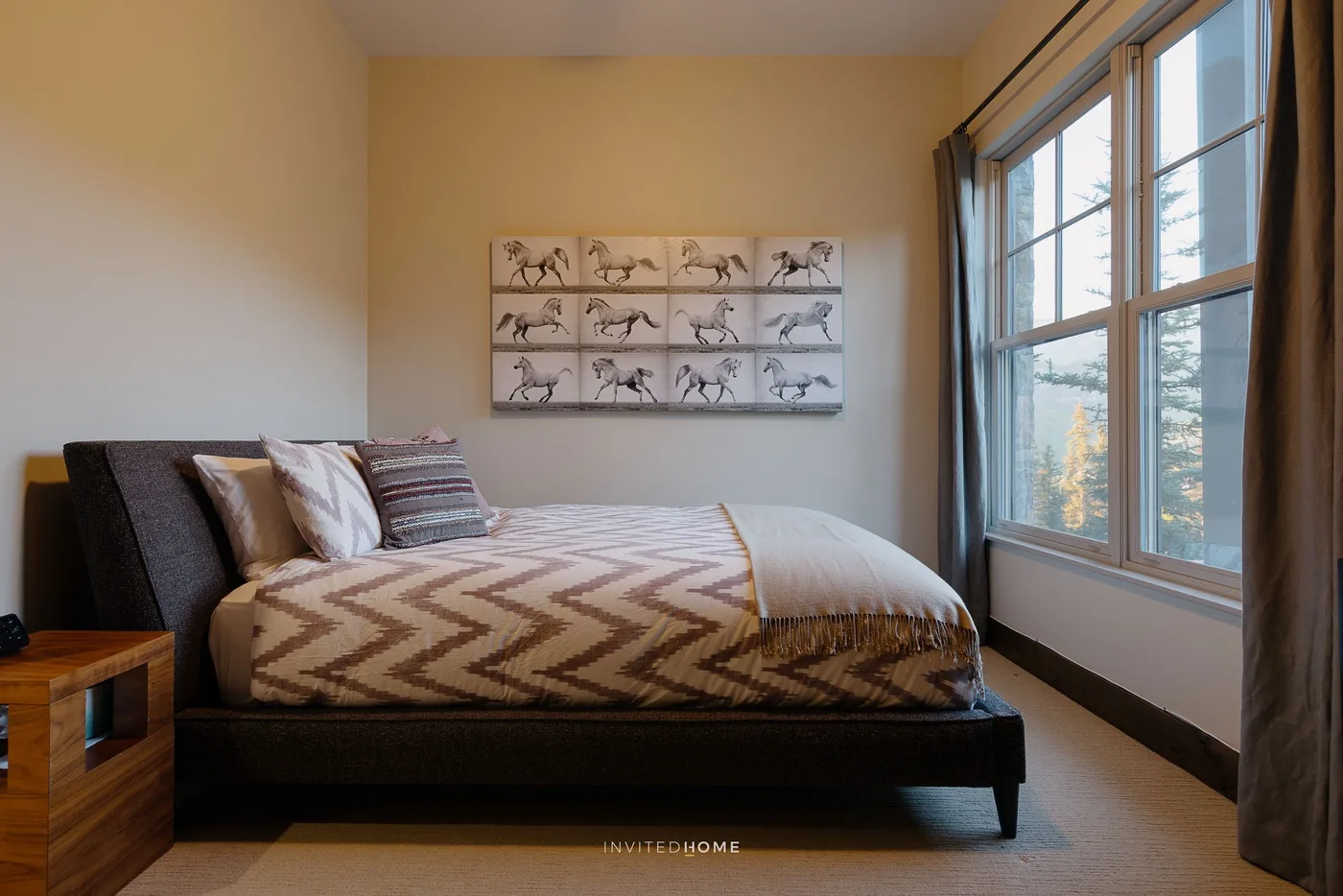 A bedroom with a bed beside large windows and framed artwork.