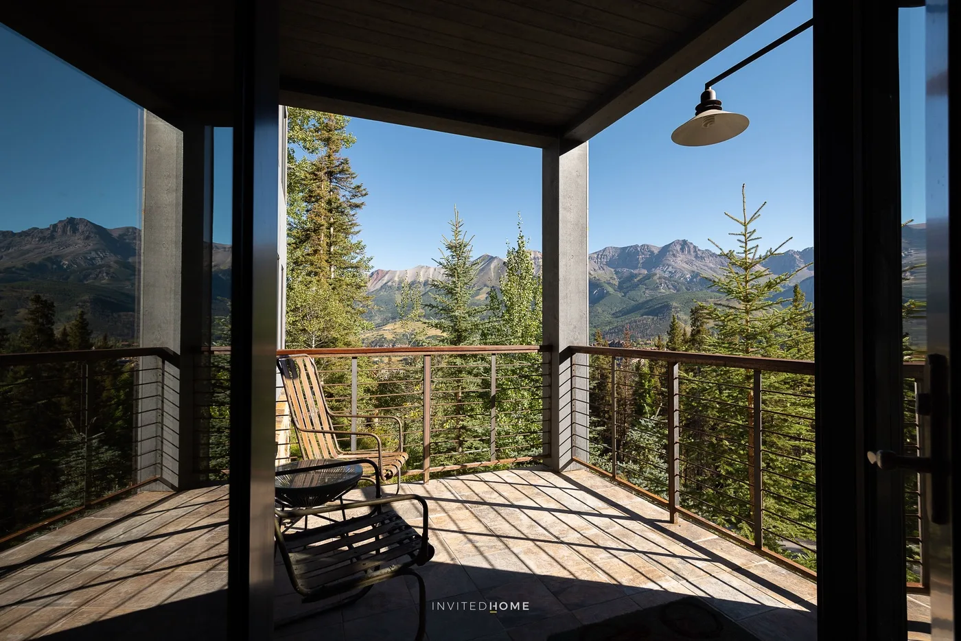 A covered outdoor deck with seating overlooks trees and distant mountains.