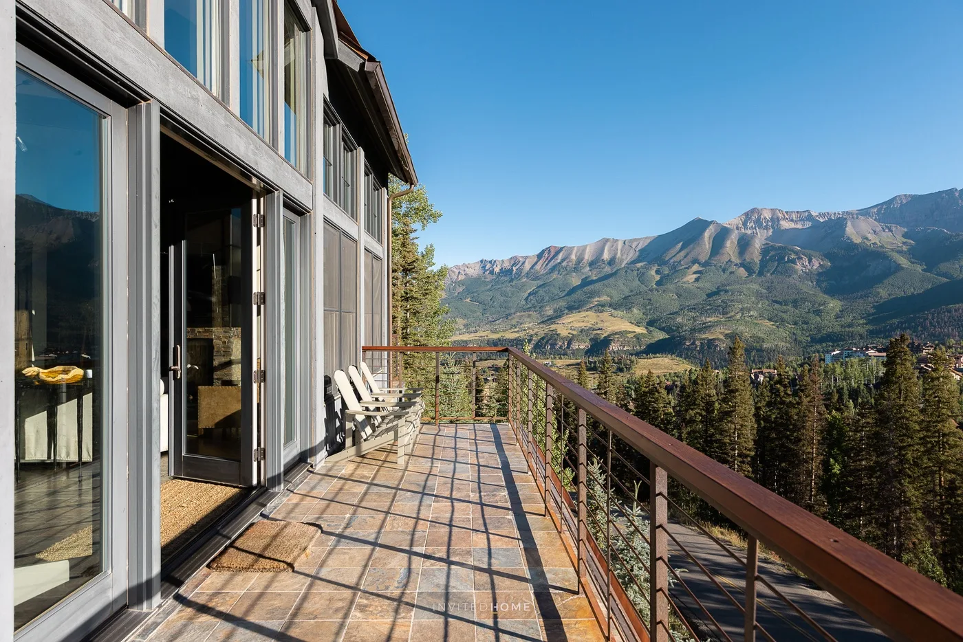 A tiled outdoor terrace beside large windows overlooks a mountain landscape.
