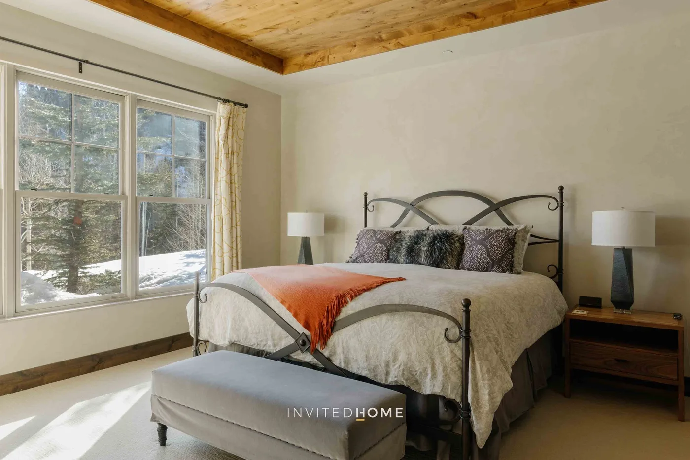 A bedroom with a metal bed, a large window, and a cushioned bench.