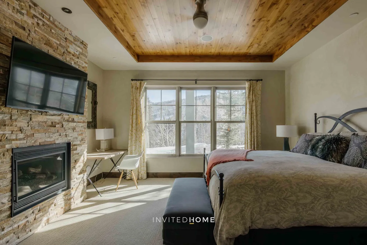 A bedroom with a large bed, a window, and a stone fireplace.