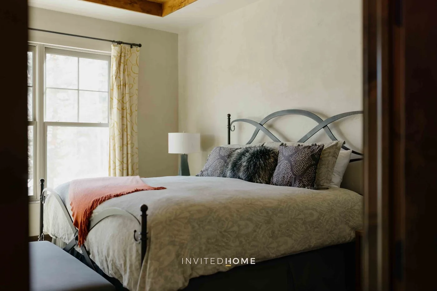 A bedroom with a neatly made bed beside a bright window.
