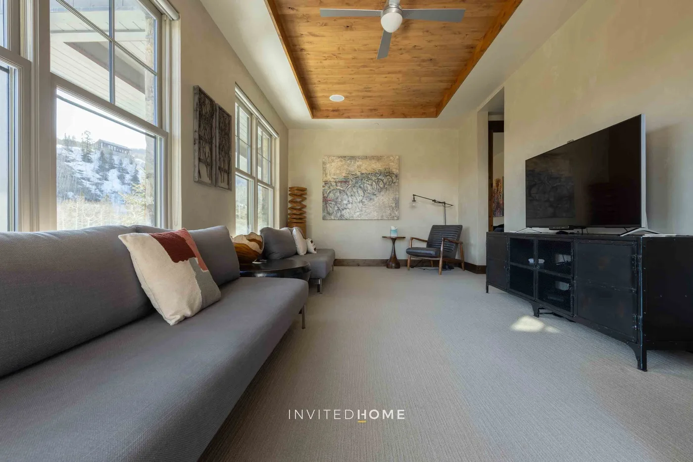A living room with seating, a television, and large windows.