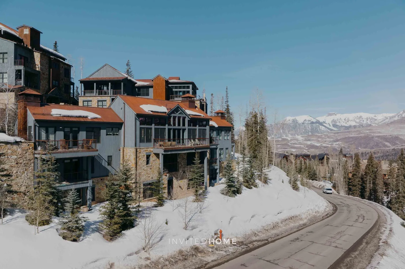 Snow-covered mountain residences line a curving road beneath a clear blue sky.