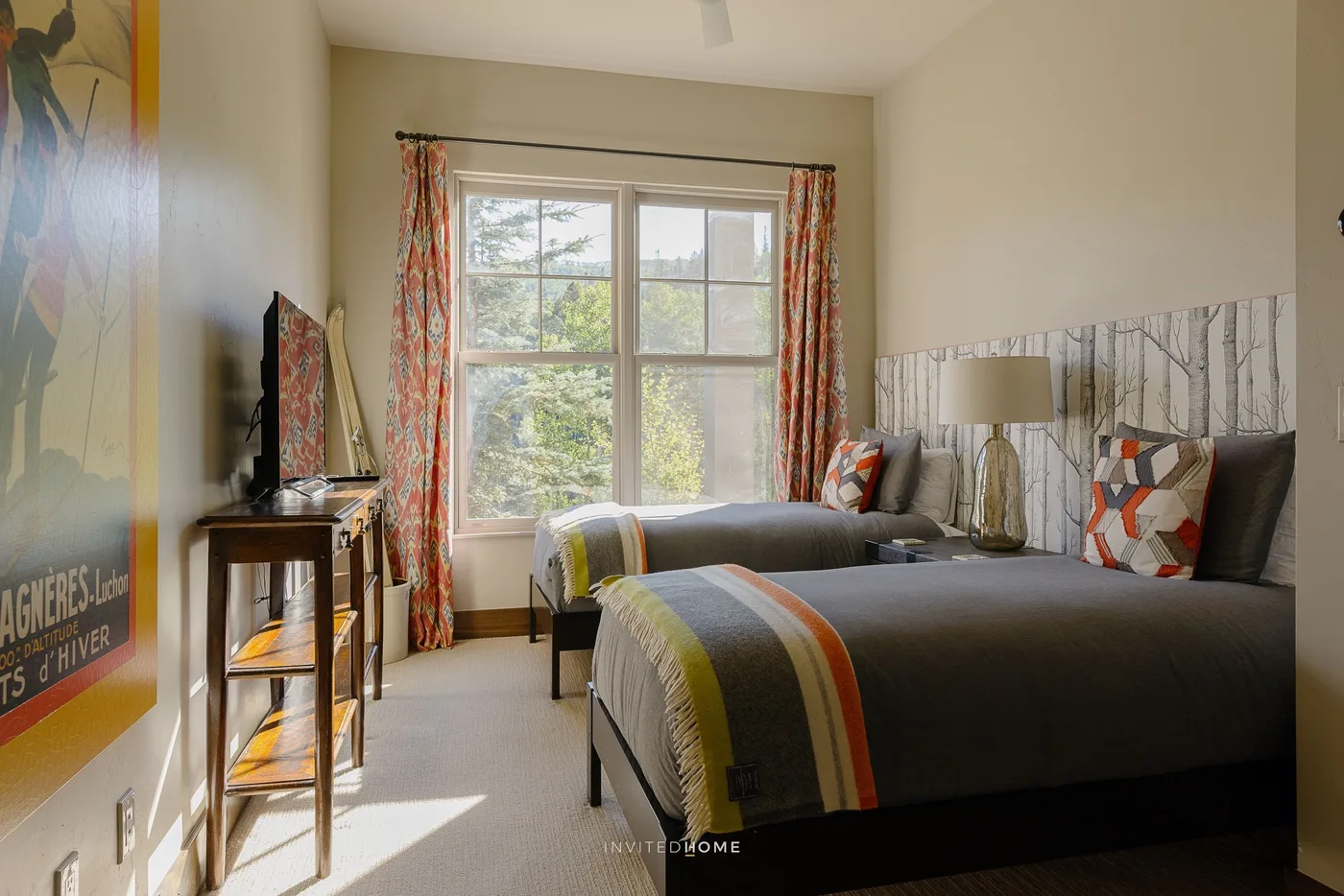 A bright bedroom with two beds, colorful curtains, and a large window.