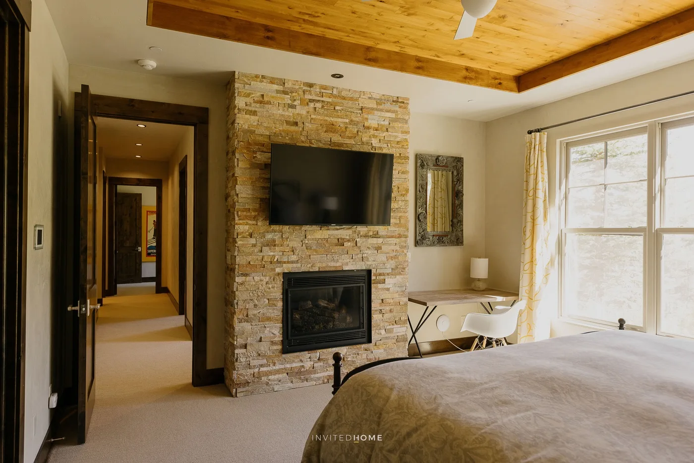 A bedroom with a bed, a stone fireplace wall, and a television.