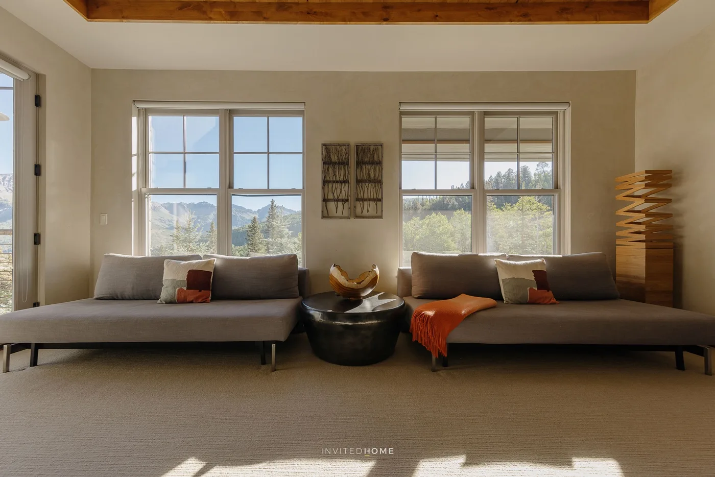 A bright living room with low seating beneath two large windows.
