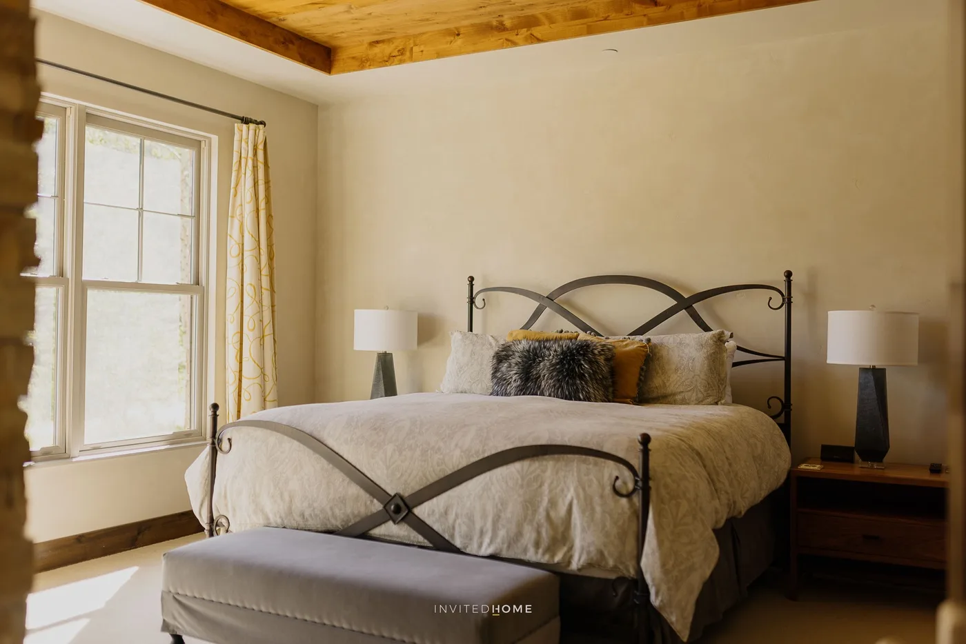 A bedroom with a bed beneath a wooden ceiling and a window beside it.
