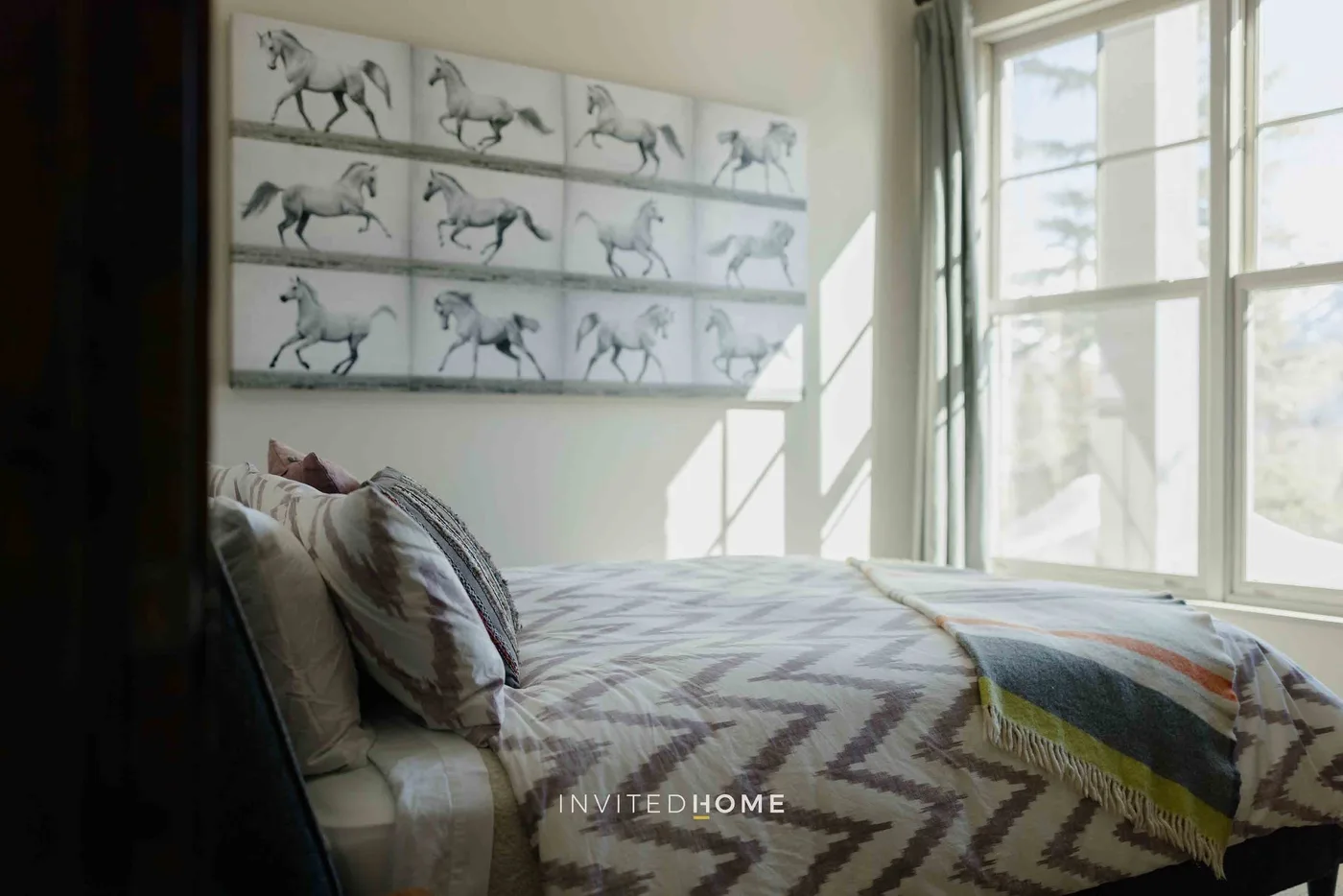 A bedroom with a patterned bed beneath framed horse artwork.