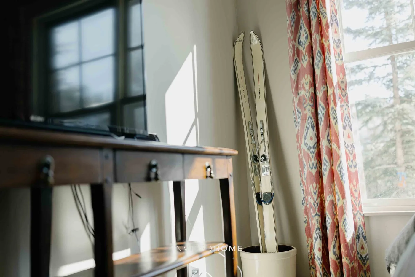 A bright living area with a television, upright skis, and patterned curtains.