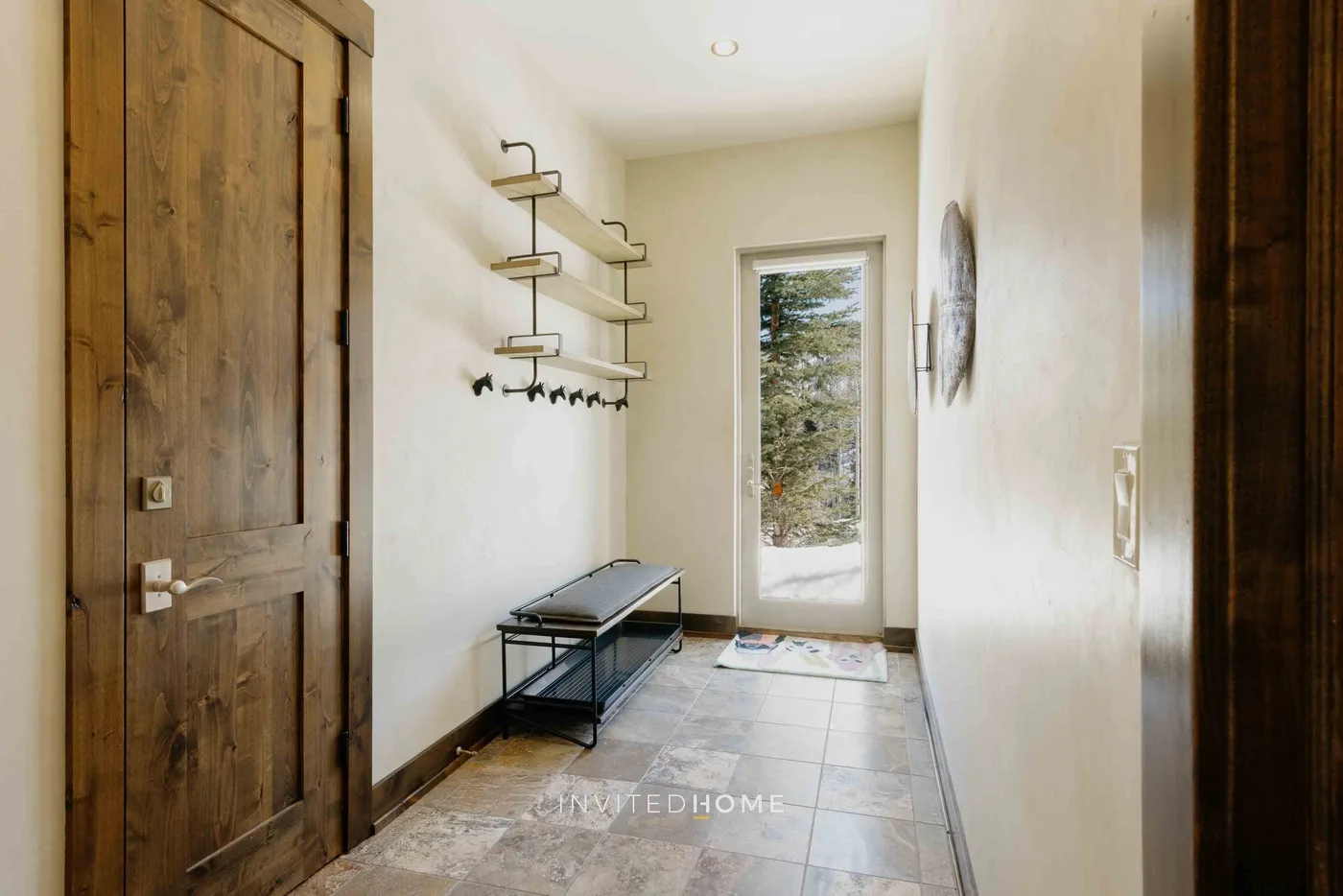 A narrow entryway with a wooden door, wall shelves, and a bench.