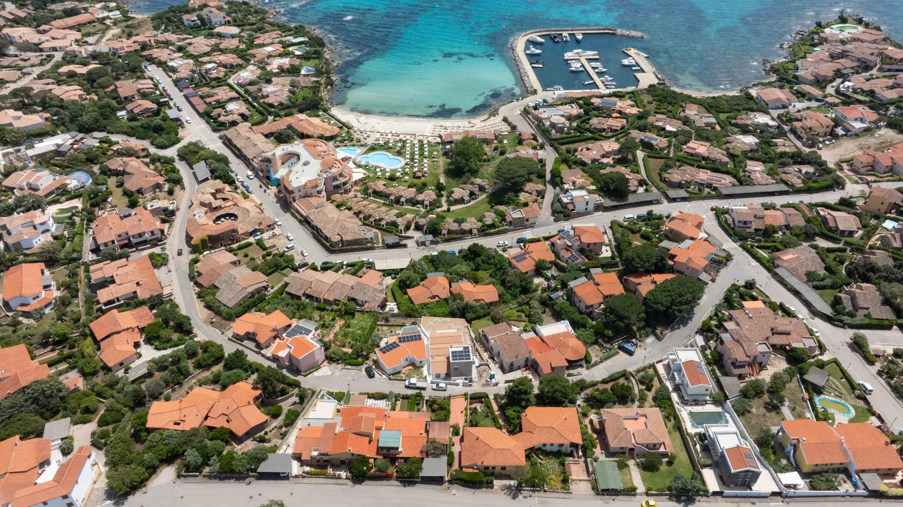 An aerial view of coastal homes, a small beach, and a marina.
