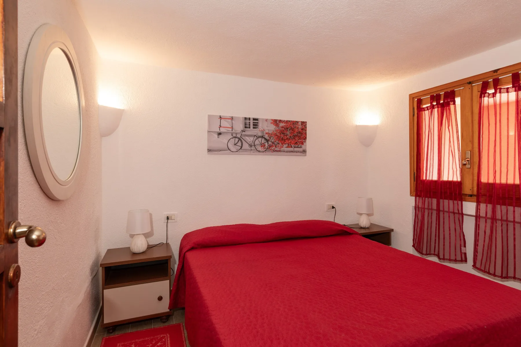 A bedroom with a red bed, bedside tables, and red curtains.