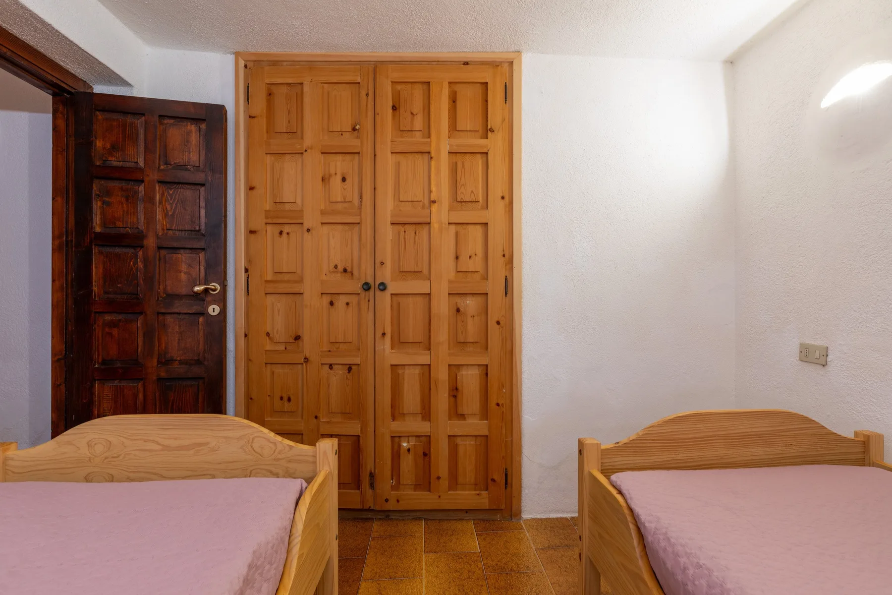 A bedroom with two beds and wooden doors against a white wall.