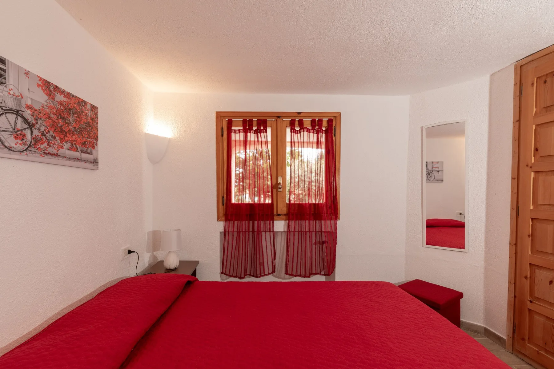 Bedroom with a red bed and sheer curtains over the window.