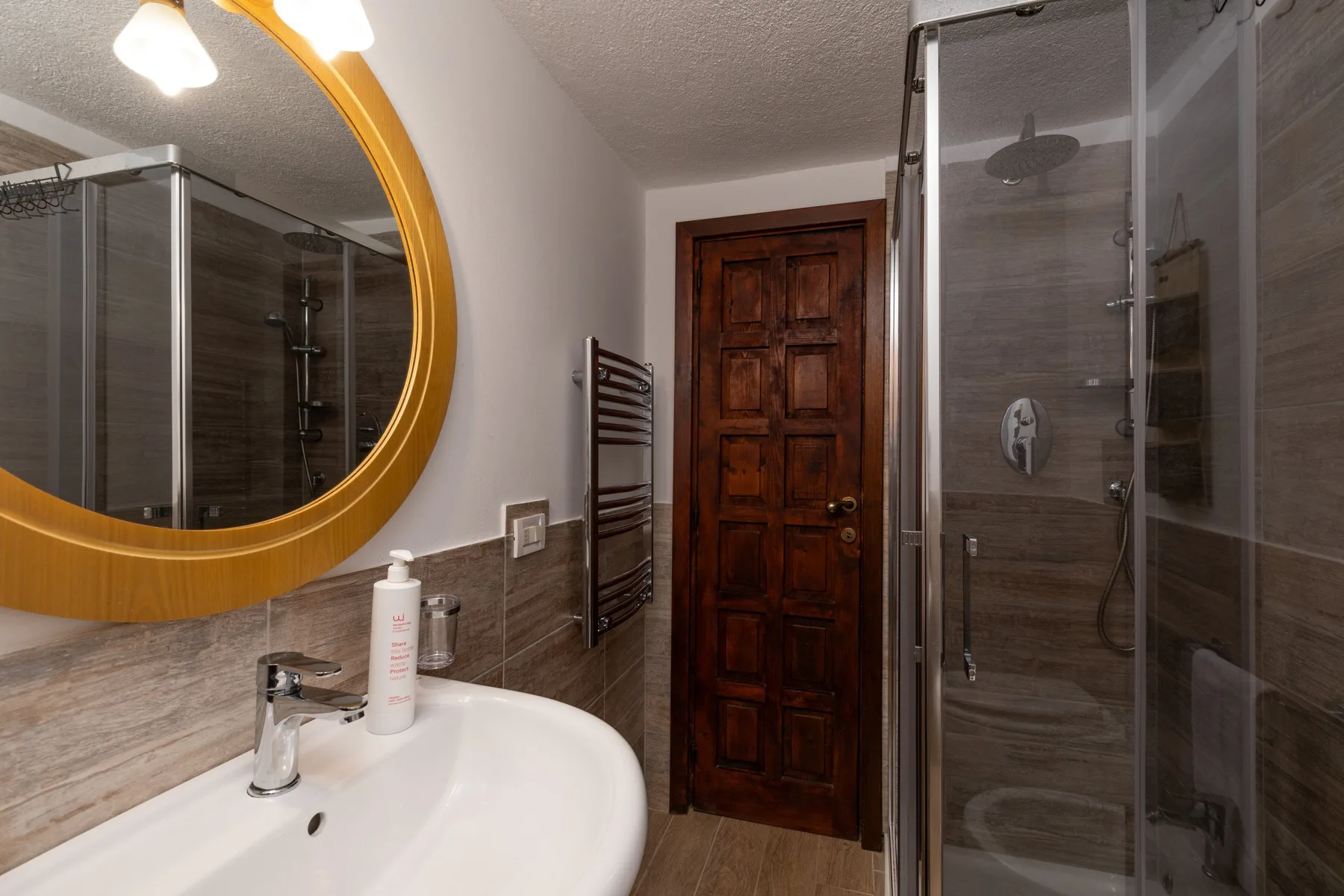 A bathroom with a sink, round mirror, and glass-enclosed shower.