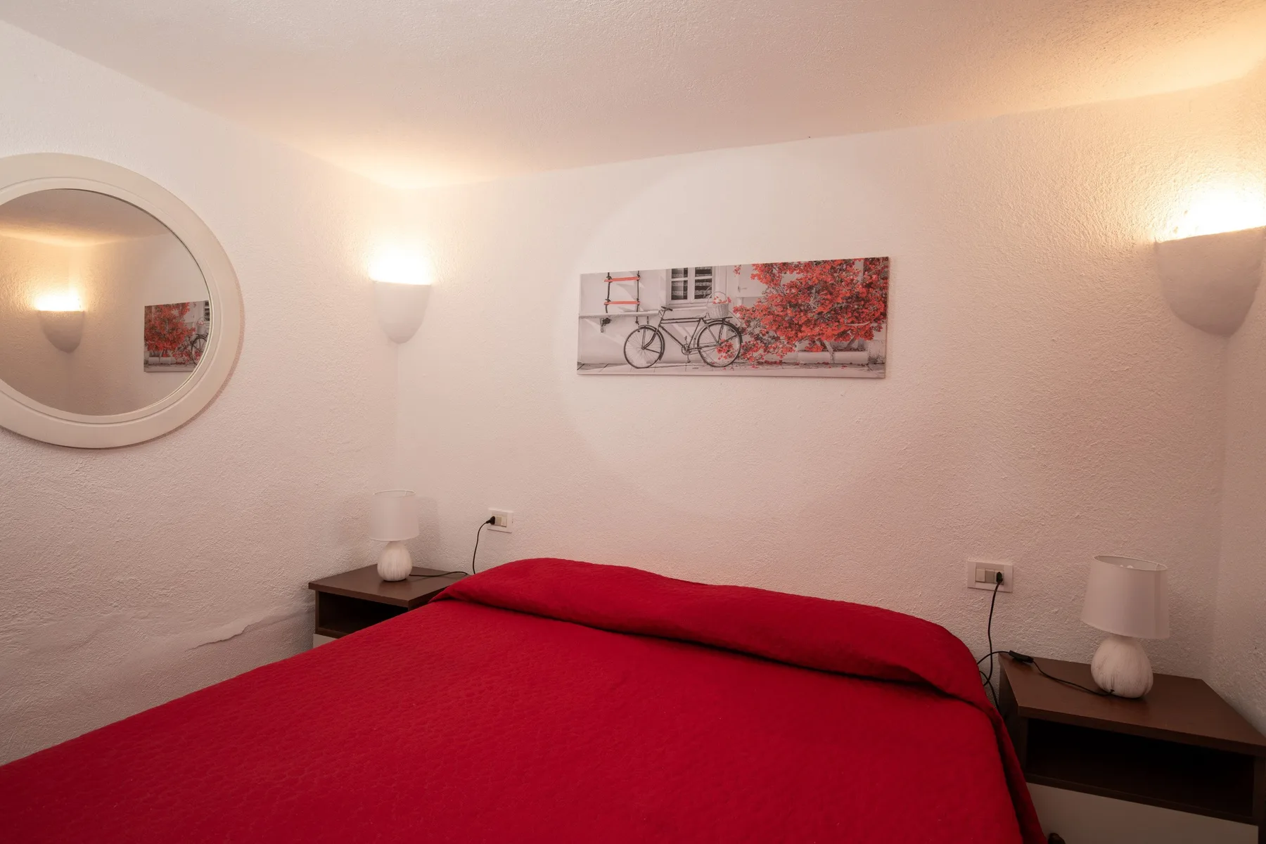 A bedroom with a red bed, bedside tables, and wall decorations.