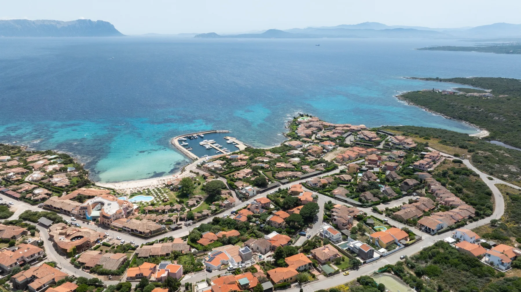 An aerial view of a coastal town beside turquoise water and a marina.