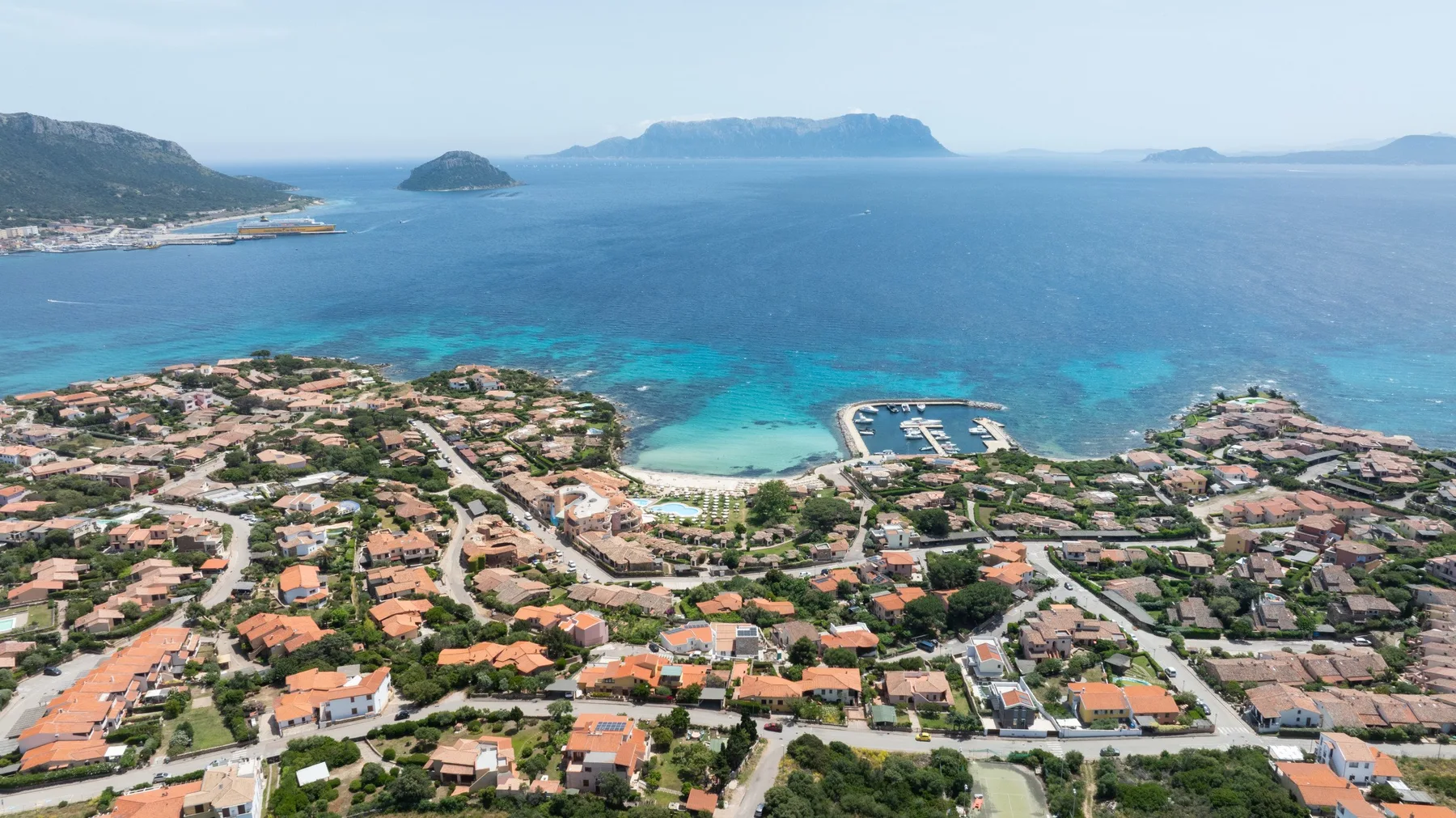 Aerial view of a coastal neighborhood beside turquoise water and a marina.