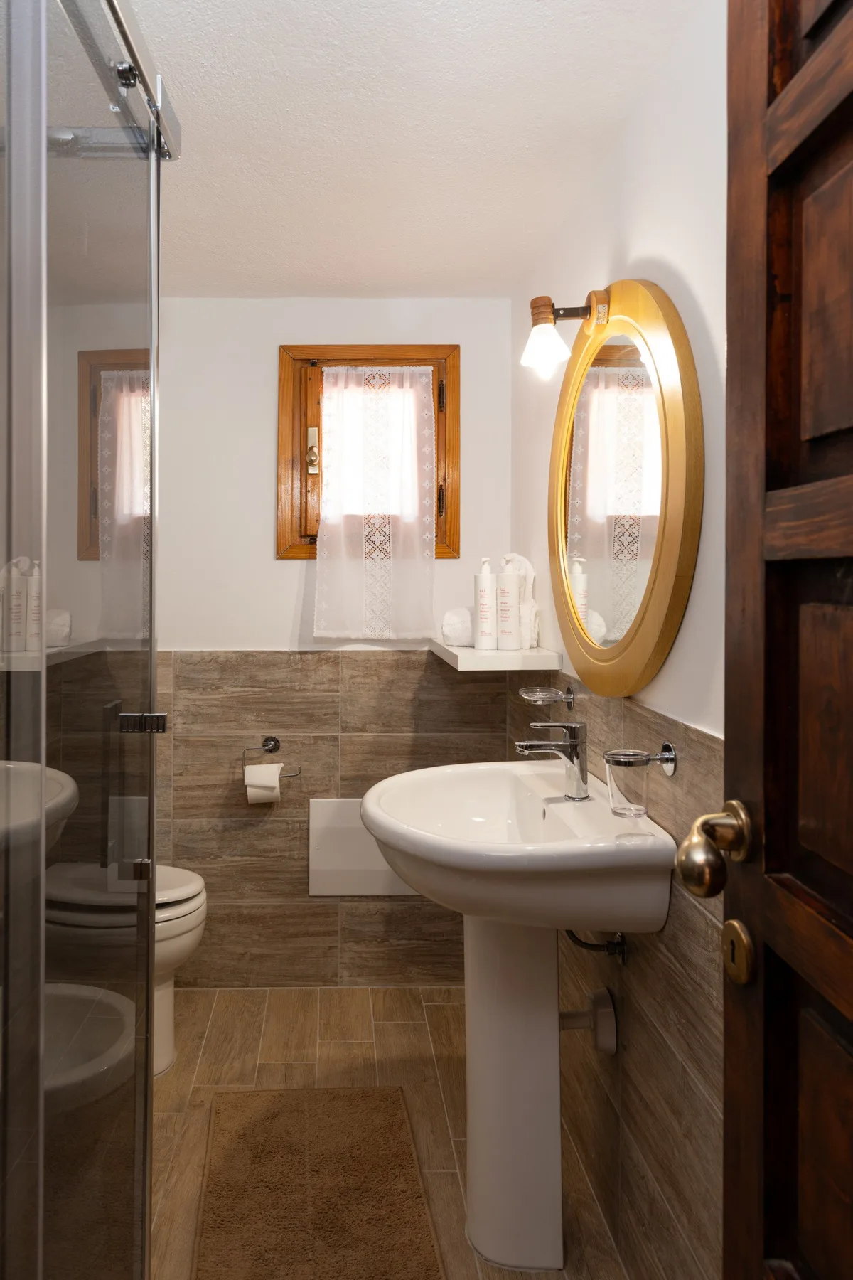 A bathroom with a pedestal sink, shower, and small window.