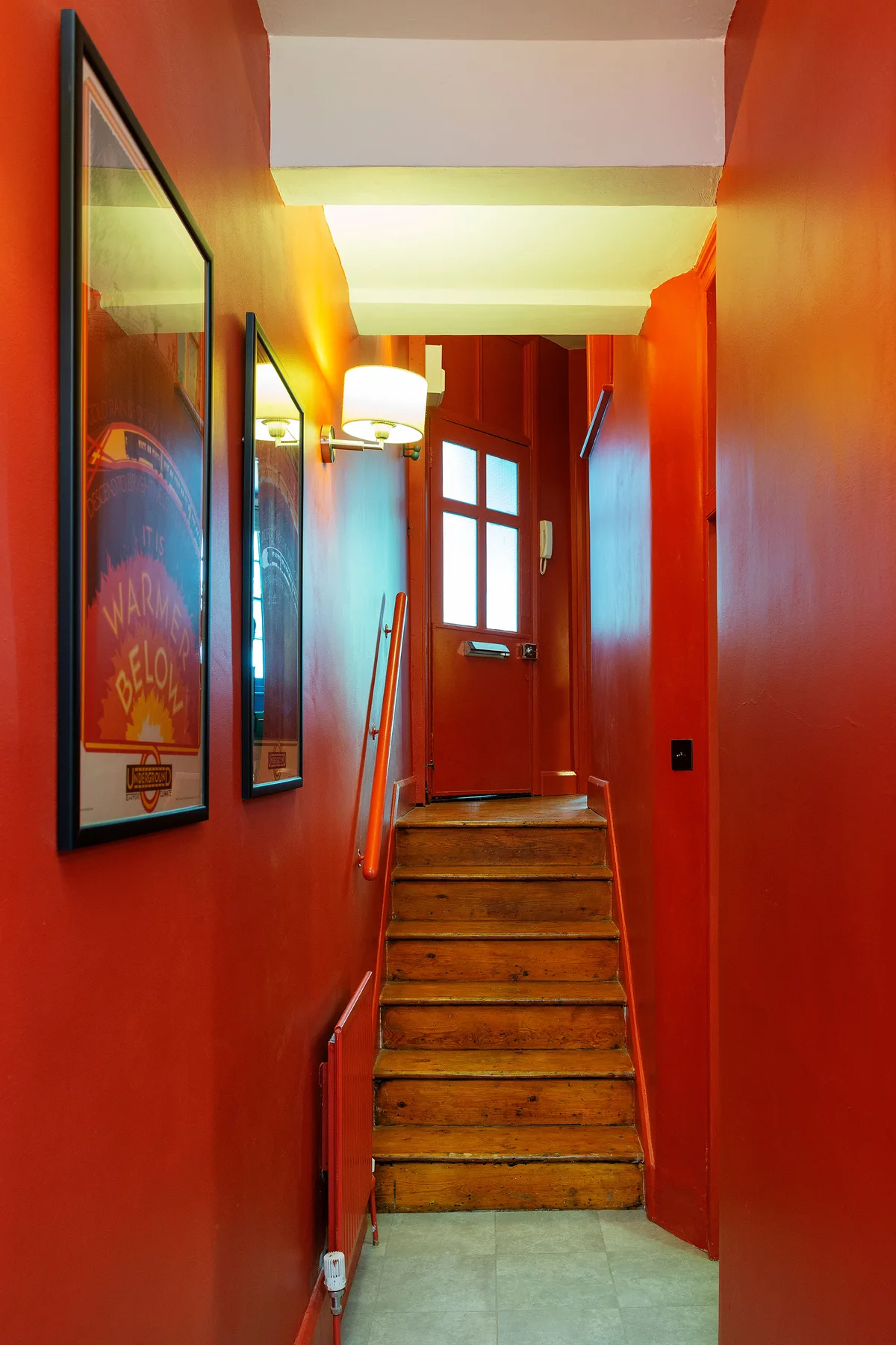 Un pasillo estrecho y rojo conduce a una escalera de madera y una puerta con paneles de vidrio.