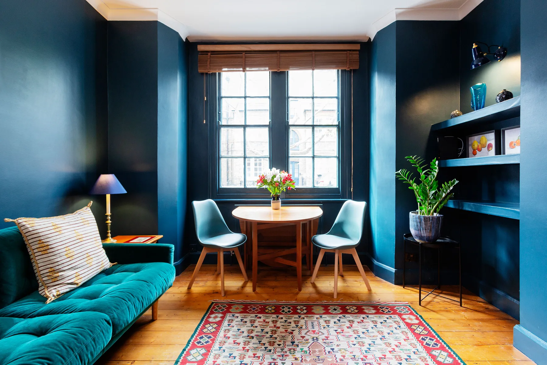 Una sala colorida con un sofá turquesa, una mesa pequeña y una ventana grande.