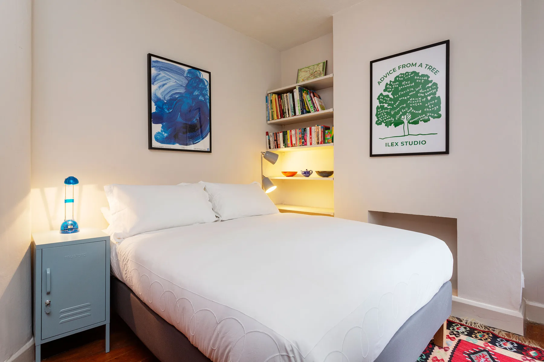 Un dormitorio con una cama tendida, cuadros enmarcados y estanterías con libros.