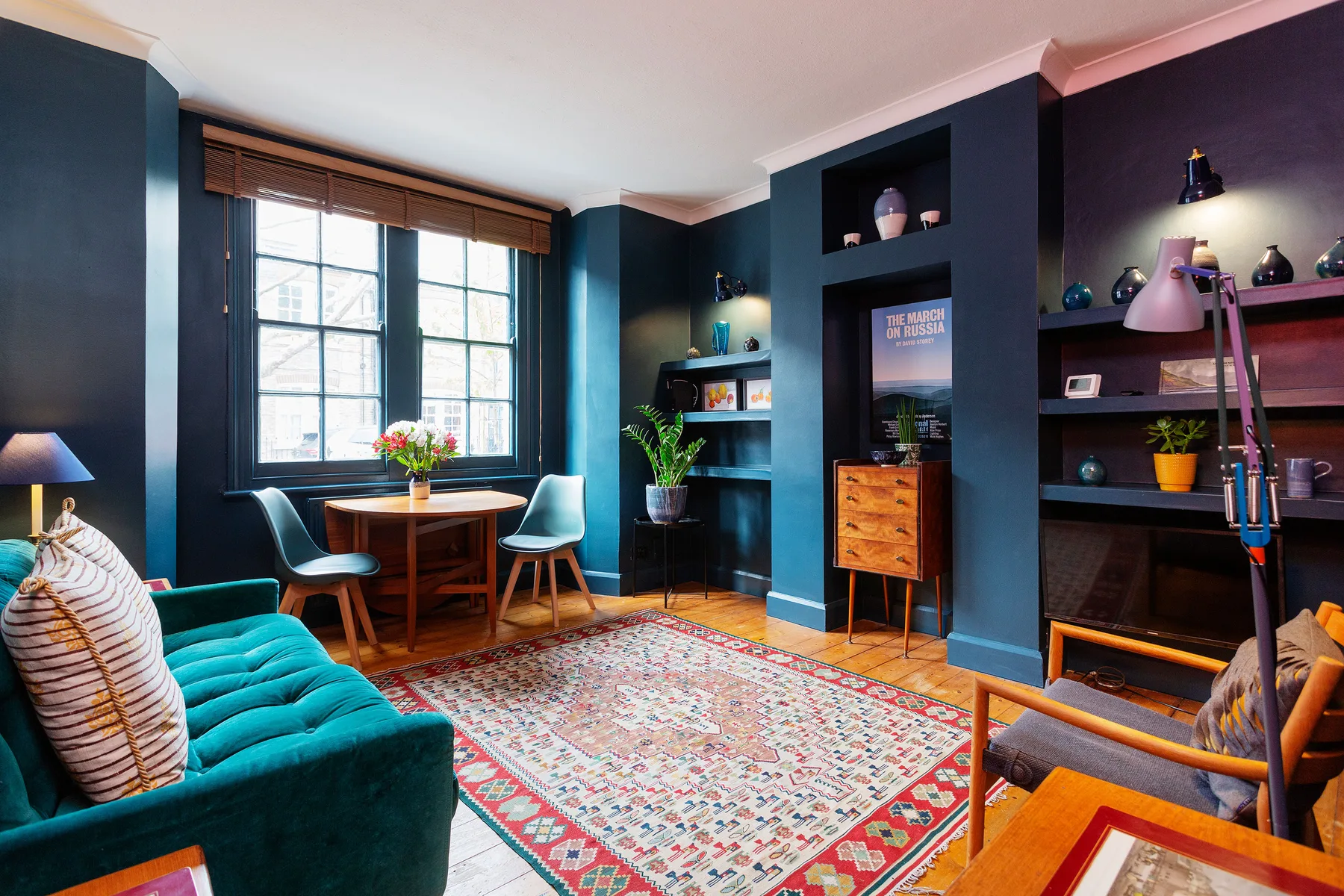 Una sala colorida con un sofá turquesa, una alfombra estampada y una ventana grande.