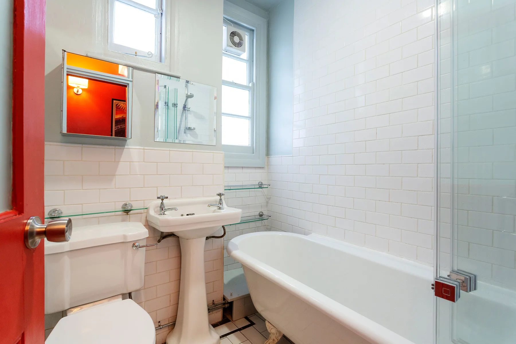 Un baño luminoso con azulejos, bañera, lavabo de pedestal y ventana.