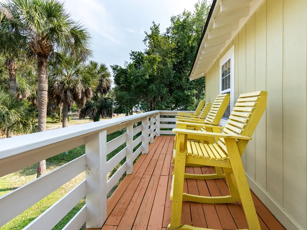 A wooden deck with yellow seating overlooks a row of palm trees.