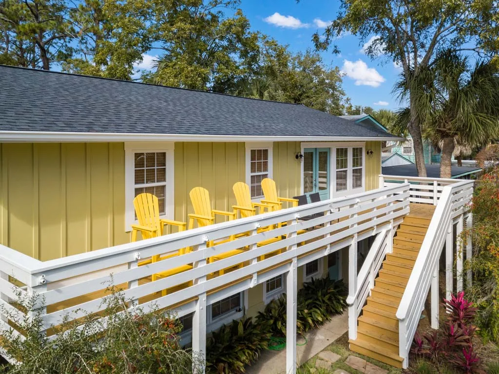 A yellow house with a raised deck, white railings, and bright outdoor seating.