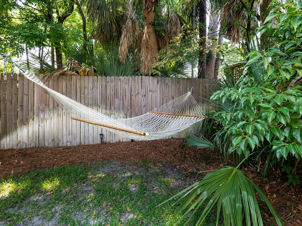 An outdoor garden with a hammock suspended between trees beside a wooden fence.