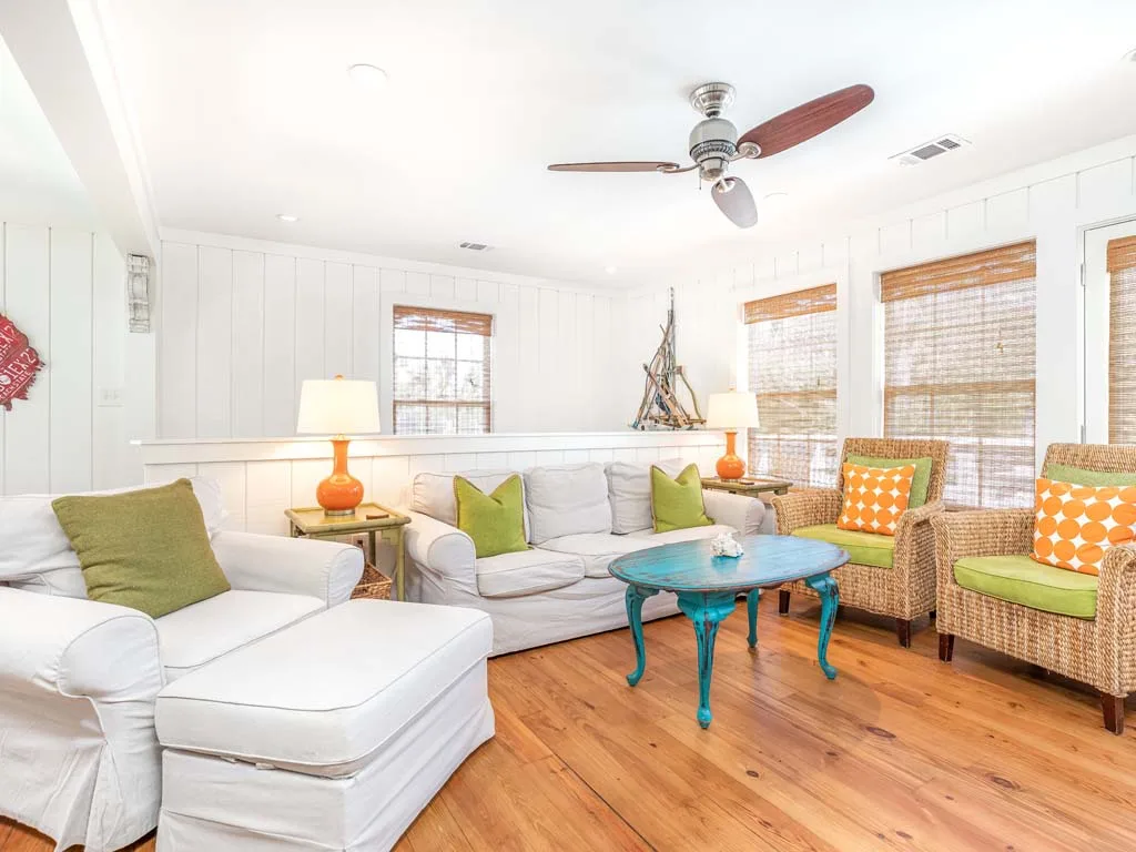 A bright living room has white seating, wicker chairs, and a turquoise coffee table.