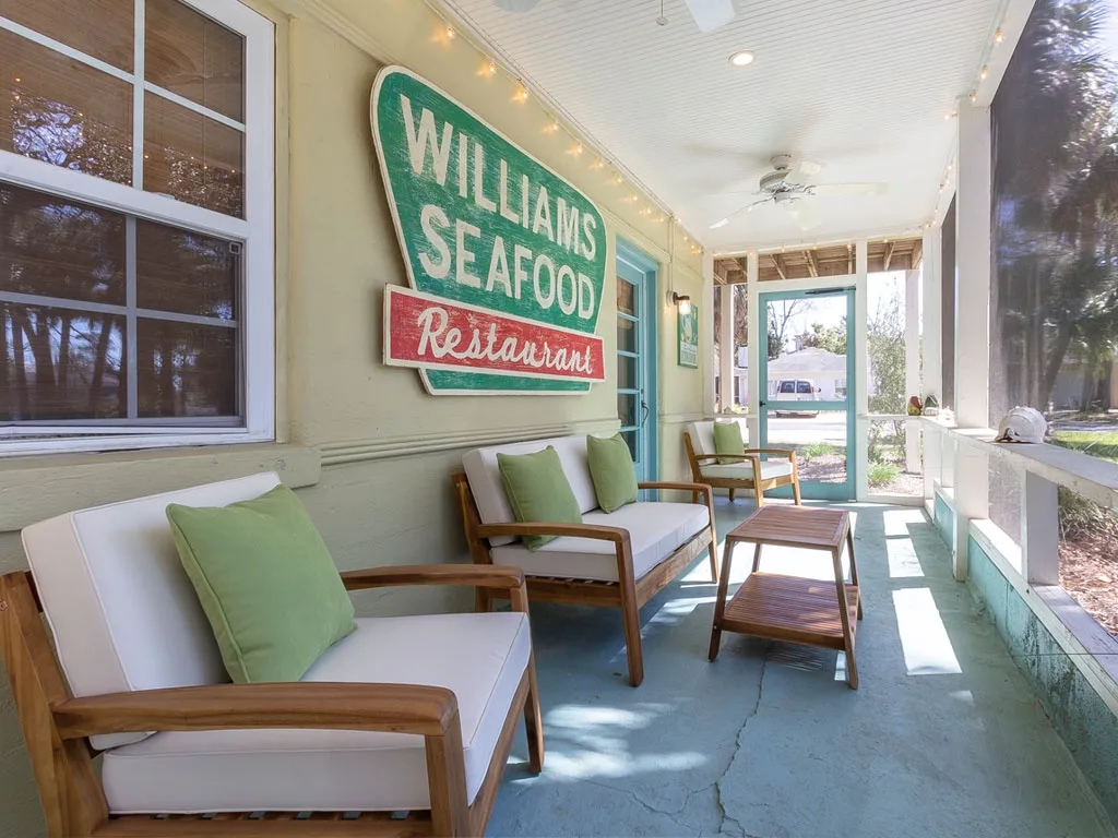 A bright enclosed porch with cushioned seating and a seafood restaurant sign.