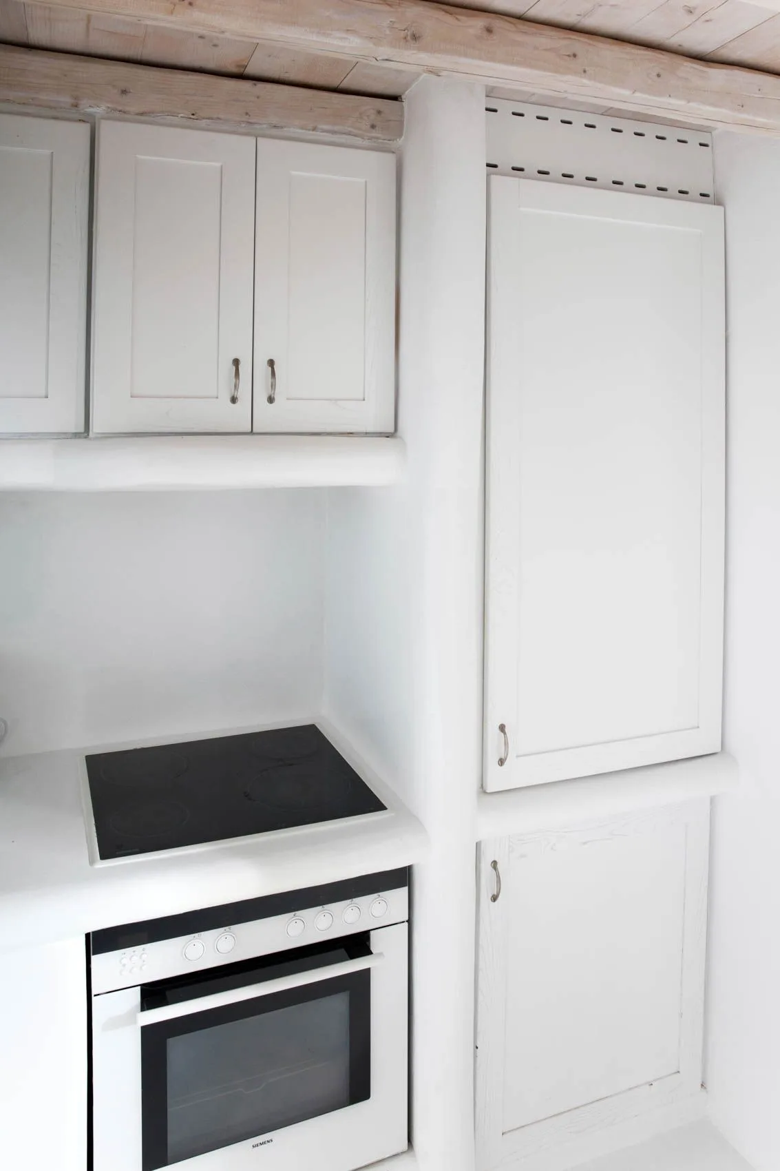 A white kitchen with built-in cabinets, a cooktop, and an oven.