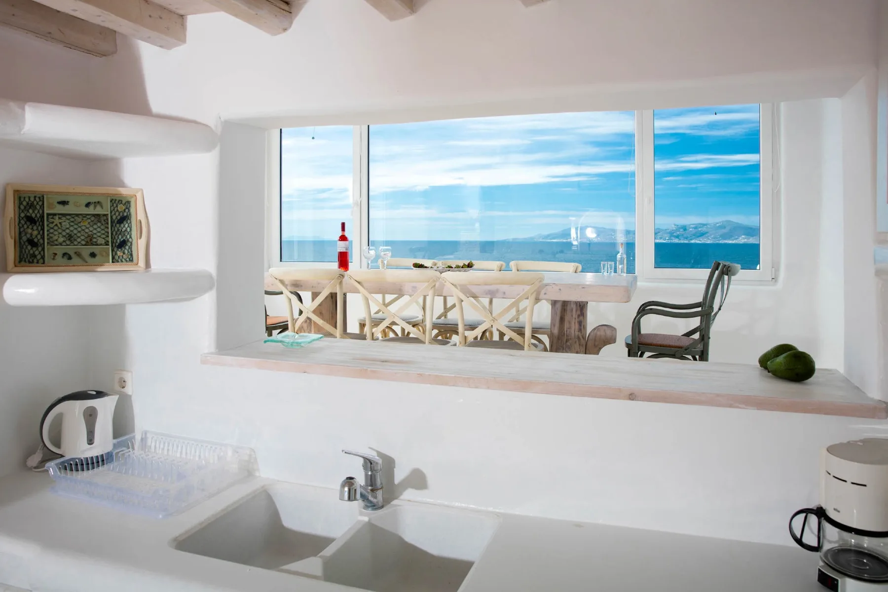 A bright kitchen with a sink and counter overlooking a dining area and ocean.