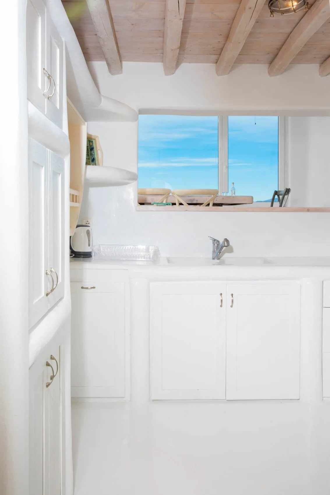 A bright white kitchen with a sink beneath a wide window.