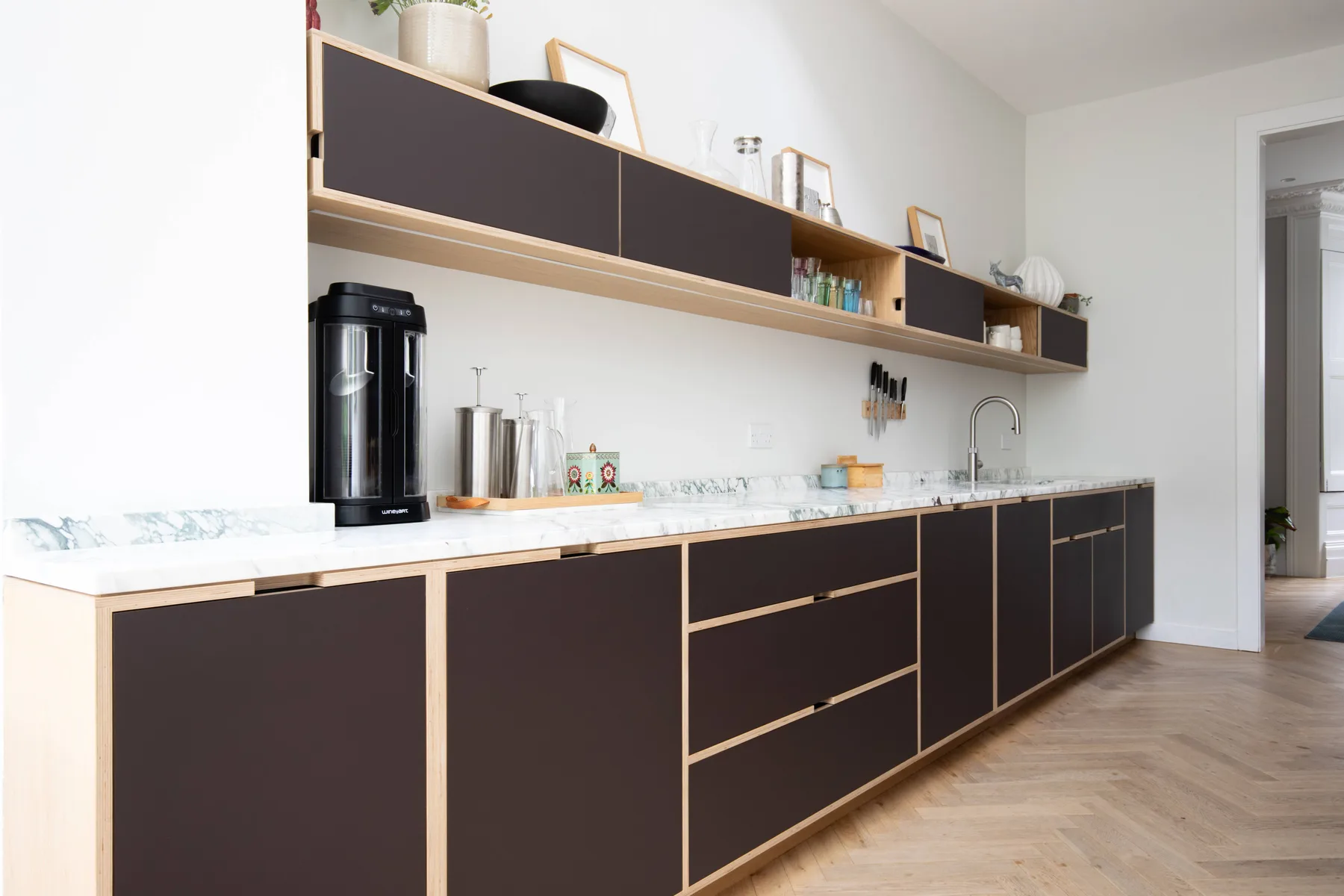A modern kitchen with dark cabinets, a long countertop, and open shelving.