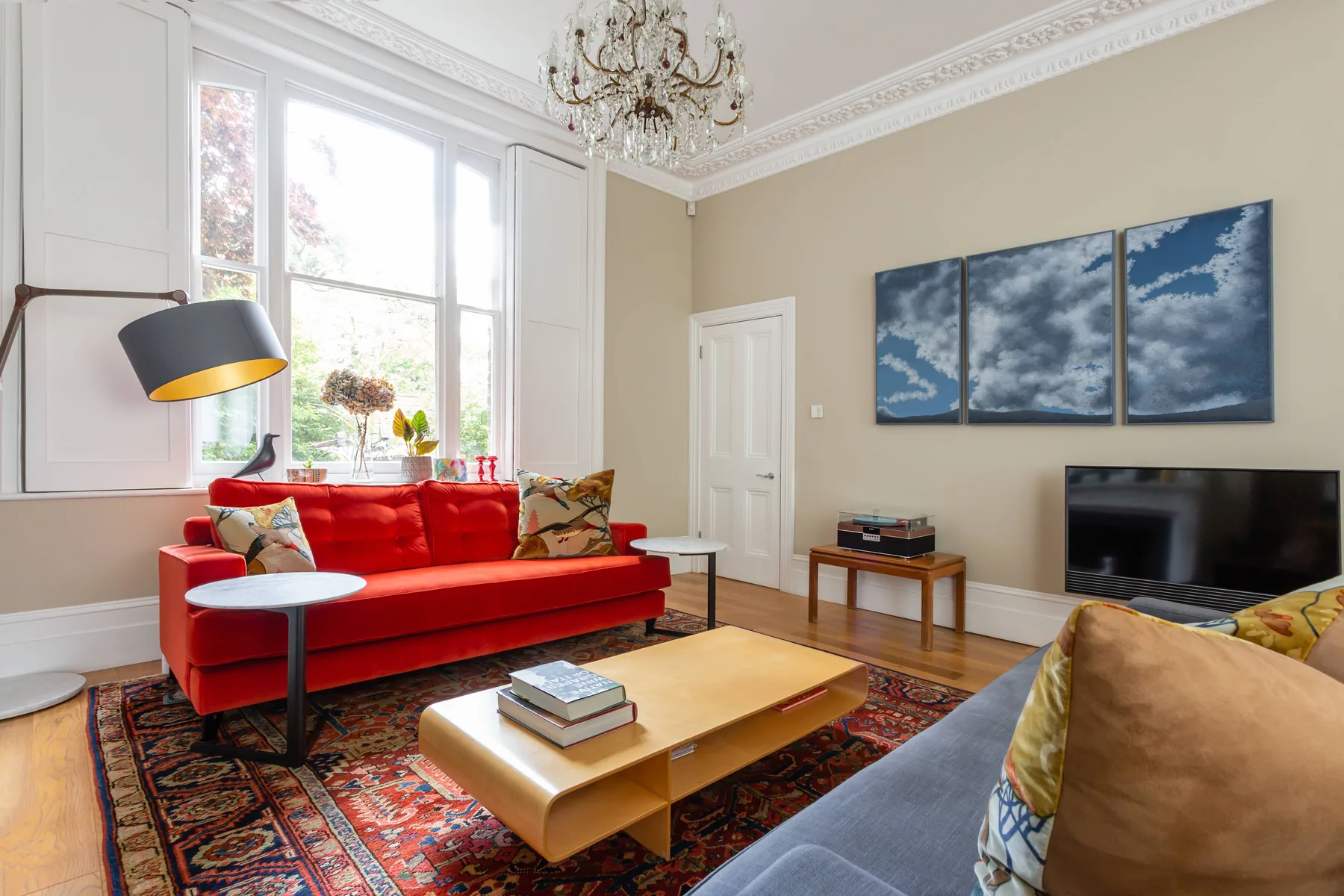 A bright living room with red seating, a coffee table, and large windows.