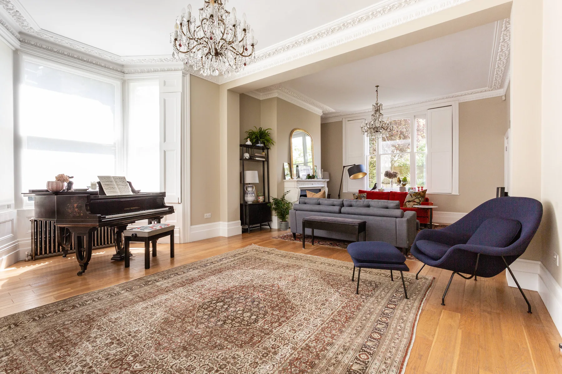 A bright living room with a grand piano, seating, and a patterned rug.