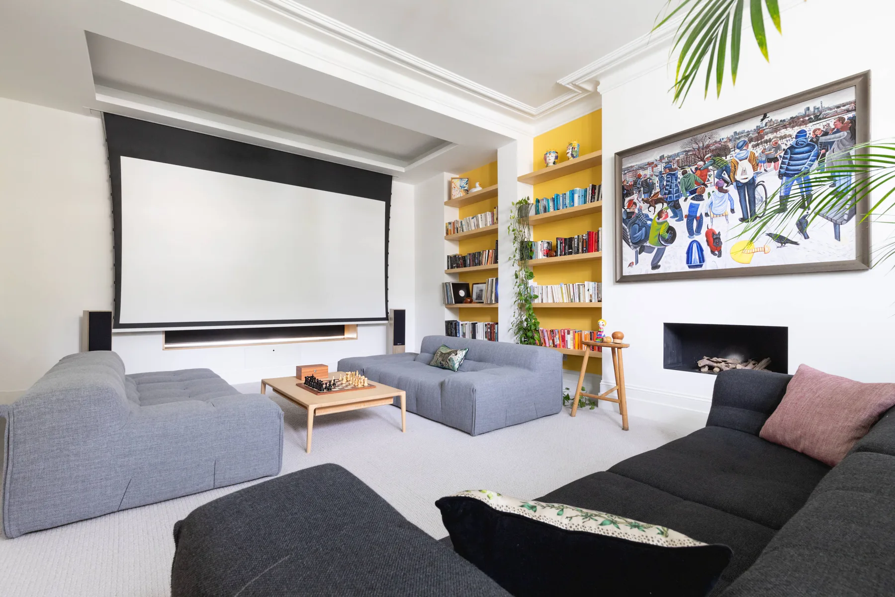 A living room with a large projection screen, seating, and colorful wall art.