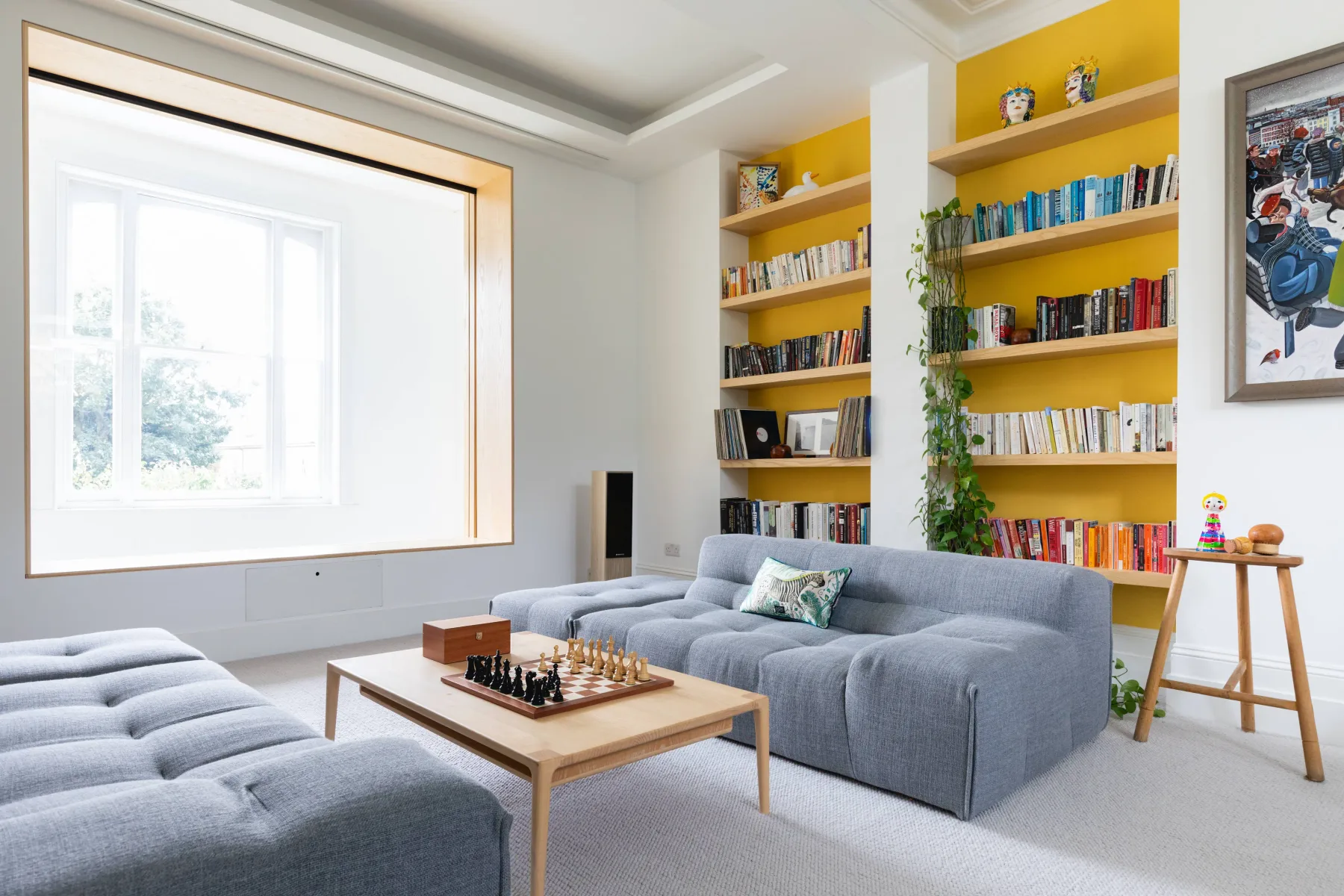 A bright living room with gray seating, a coffee table, and colorful bookshelves.