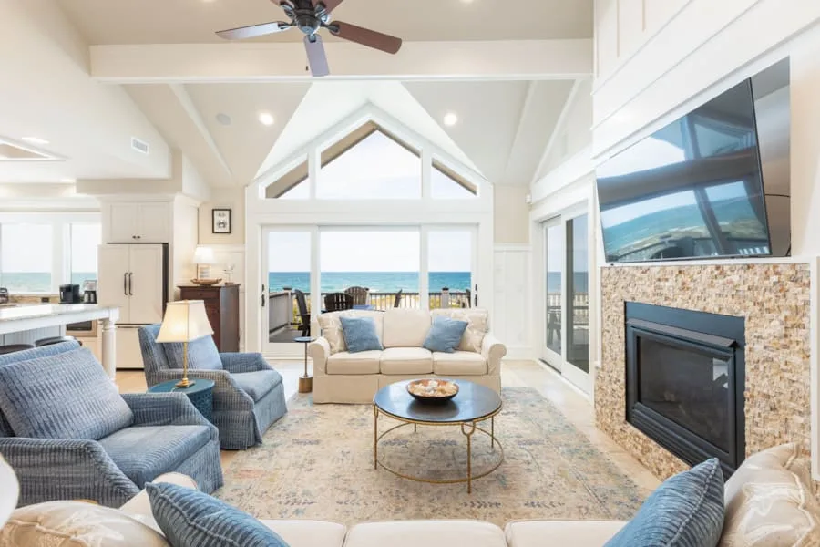 Una luminosa sala de estar con asientos, una chimenea y vistas al mar por las ventanas.