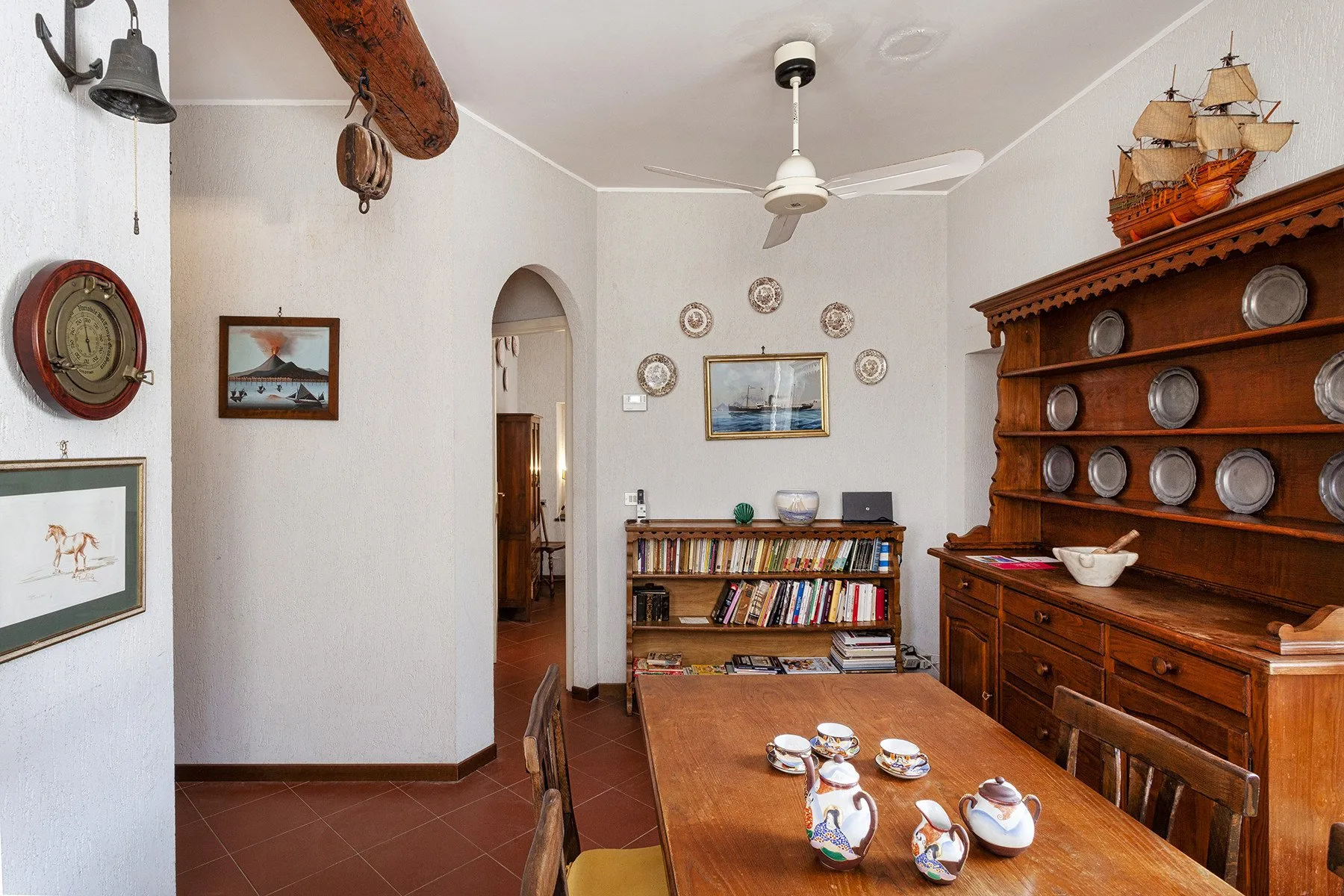 A dining room with a wooden table, decorative plates, and a bookcase.
