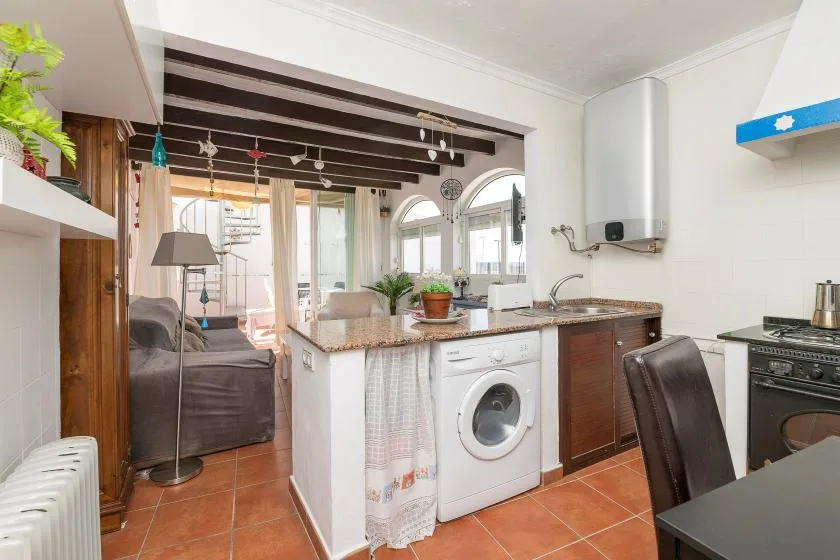 A compact kitchen with a washing machine and a seating area beyond the counter.
