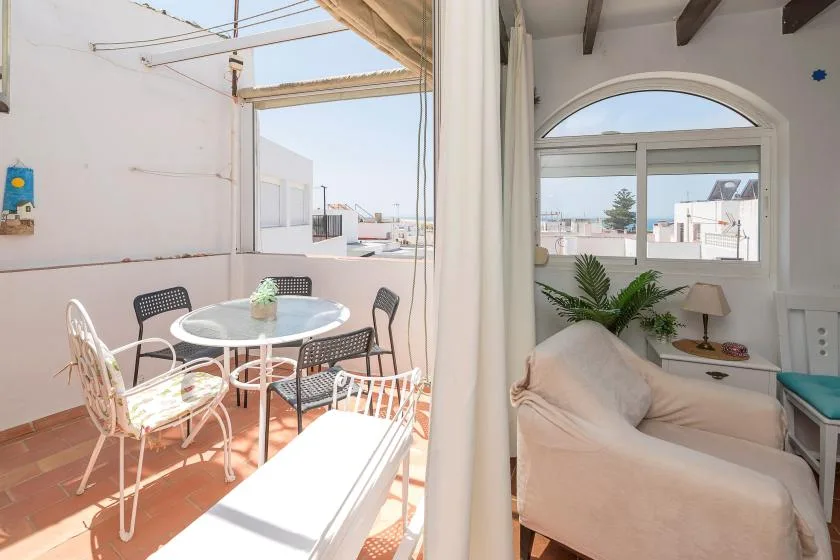 A sunlit terrace with a round table opens onto a bright sitting area.