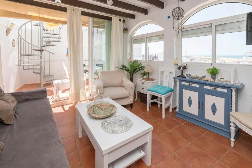 A bright living room with seating, a coffee table, and large windows overlooking the water.