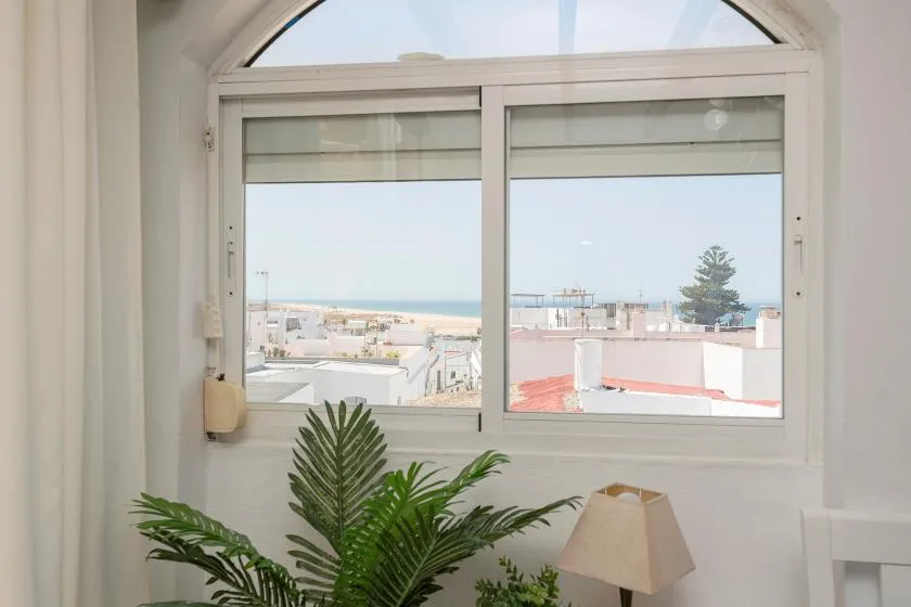 A bright room with an arched window overlooking rooftops and the sea.