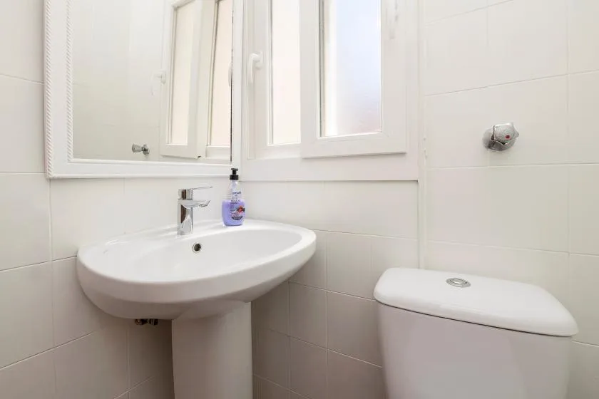 A bright bathroom with a pedestal sink and toilet beneath a window.