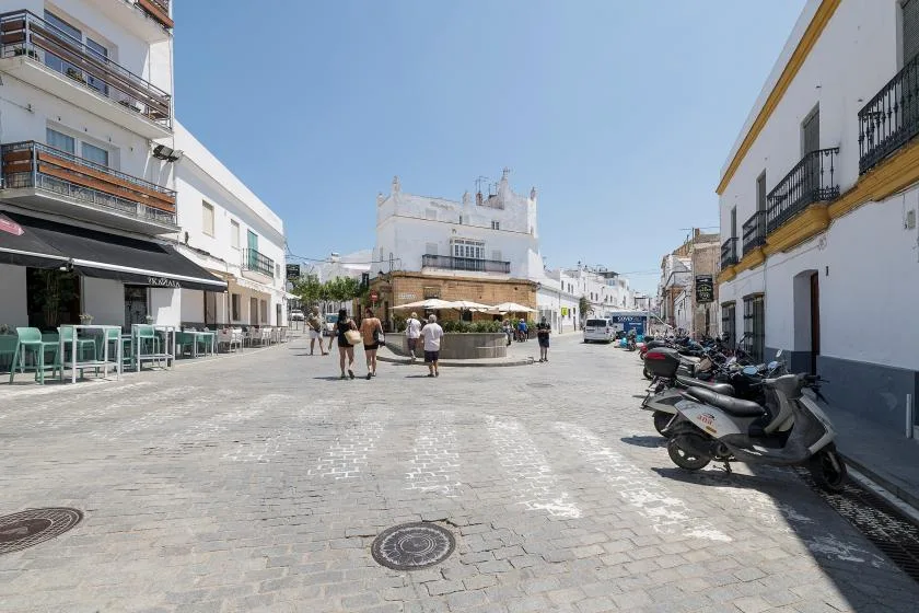 A sunny pedestrian street with outdoor café seating and parked scooters.